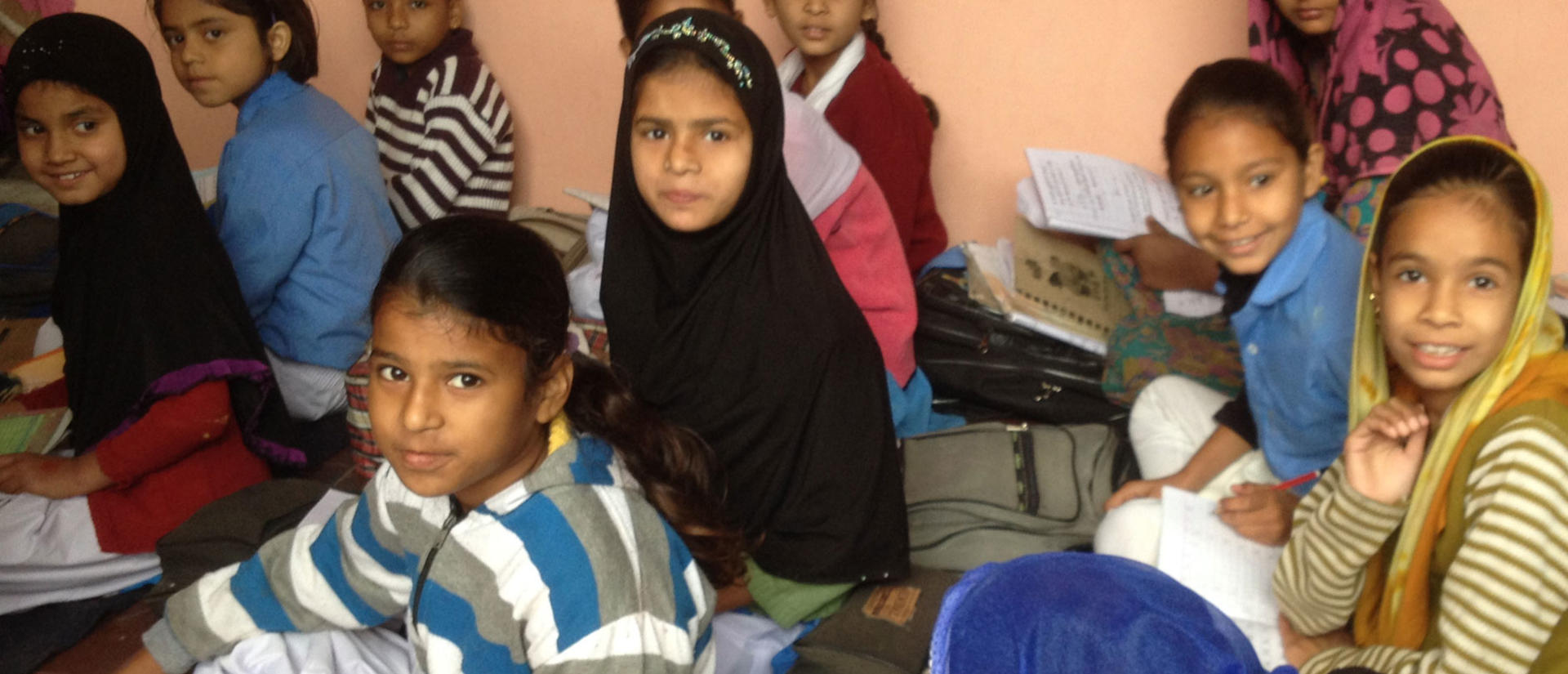 A group of international children sit on the floor and look at the camera